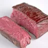 Dos trozos de arrachera de res cruda, con la fibra de la carne a la vista, sobre fondo blanco