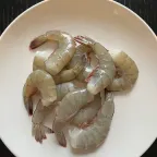 Camarones crudos sin cabeza, con su cáscara gris, sobre un plato blanco