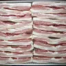 Rebanadas de tocino de cerdo crudo acomodadas en hileras sobre una charola de metal