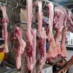 Cortes de carne de cerdo cruda colgados de ganchos en una carnicería de mercado