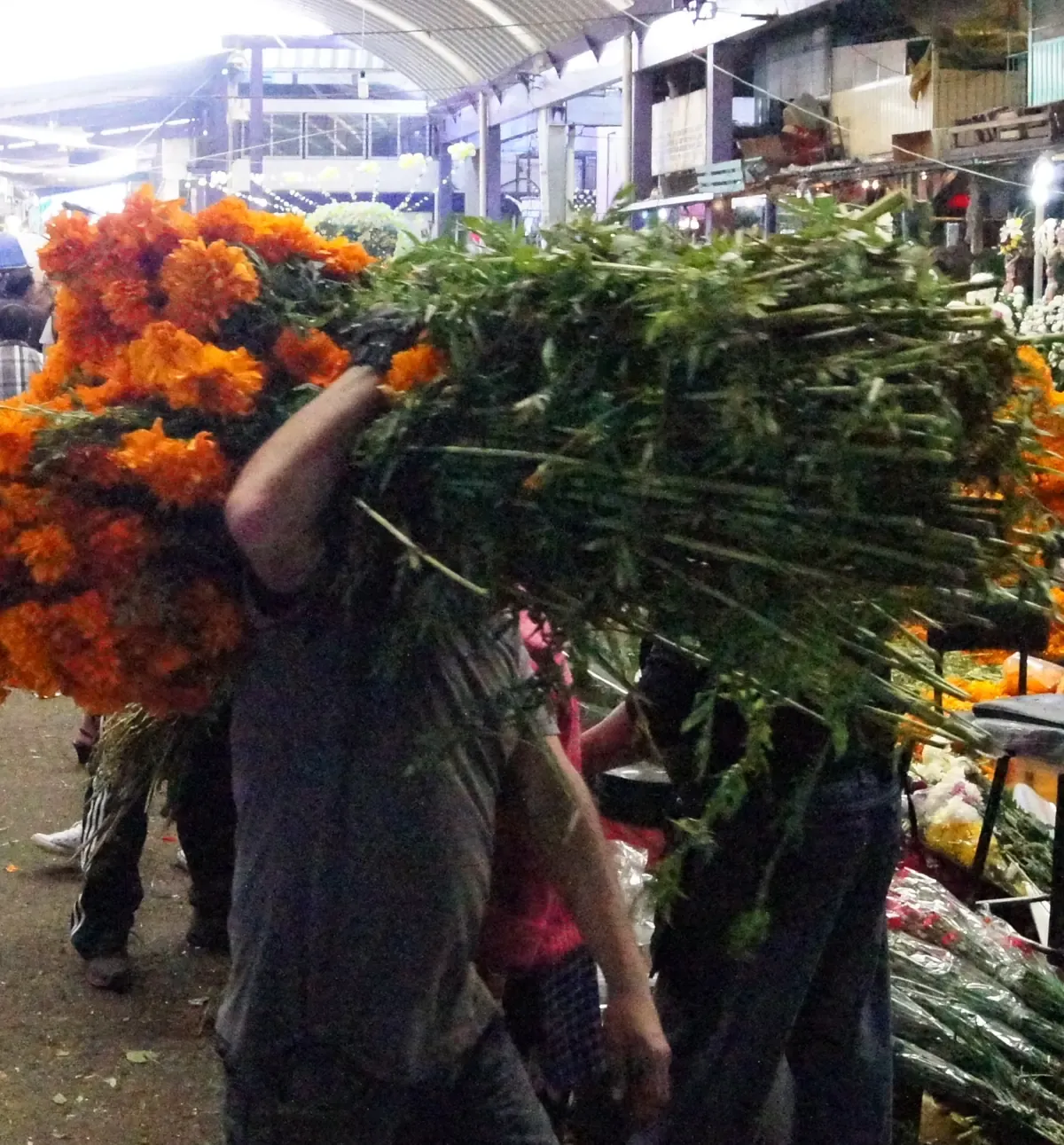 Cargador lleva un bulto de flor de cempasúchil por un pasillo del Mercado de Jamaica, en la Ciudad de México