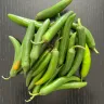 Chiles serranos verdes, delgados y alargados, apilados sobre una superficie oscura