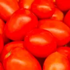 Jitomates saladette, alargados y rojos, amontonados en un puesto de mercado