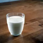 Vaso de vidrio lleno de leche blanca sobre una mesa de madera oscura