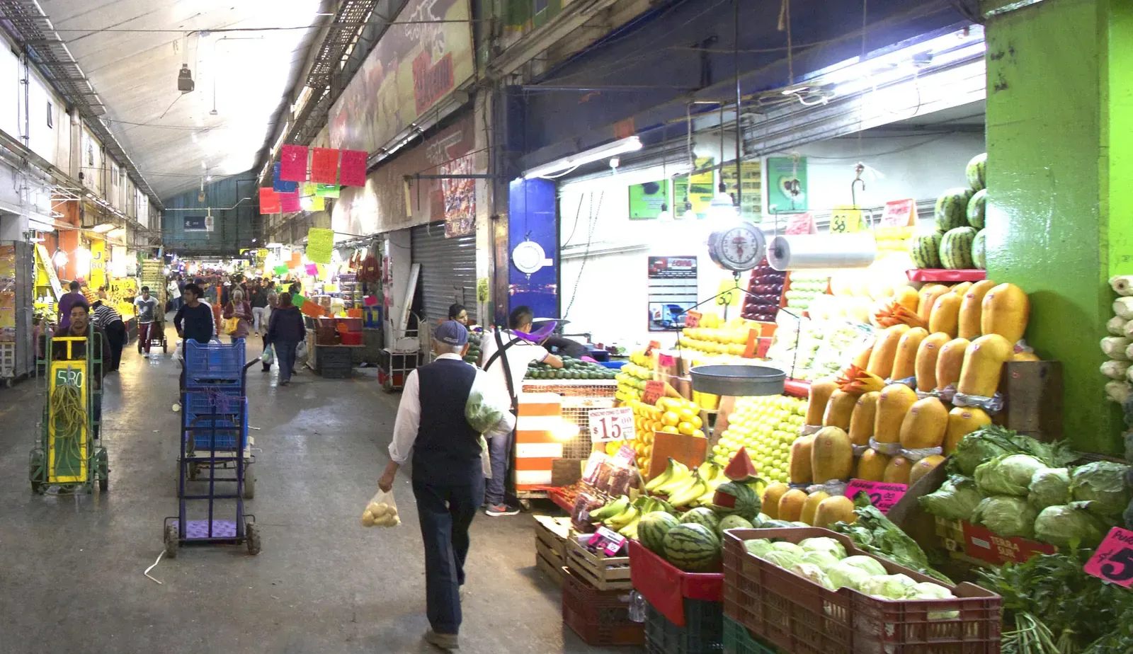 Pasillo de la Central de Abasto de la Ciudad de México con puestos de frutas y verduras y diablitos de carga