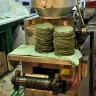 Pilas de tortillas de maíz azul recién hechas junto a la máquina tortilladora de una tortillería de mercado