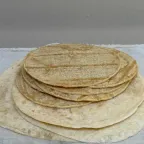 Pila de tortillas de maíz recién hechas sobre tortillas de harina más grandes, en un mantel