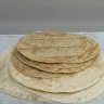 Pila de tortillas de maíz recién hechas sobre tortillas de harina más grandes, en un mantel